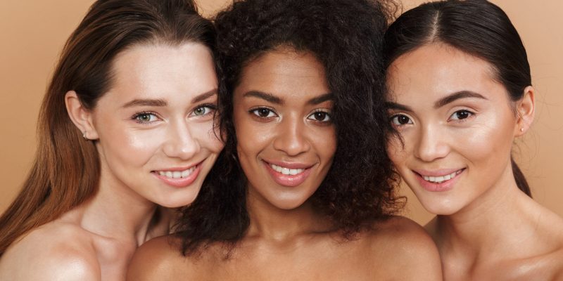 Close up image of three happy naked women posing together and looking at the camera over beige background